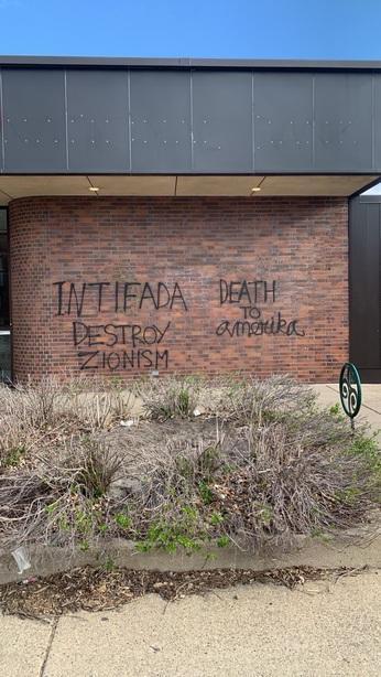 An exterior bank wall has "Intifada", "Destroy Zionism" and "Death to amerika" written on it in black spraypaint.