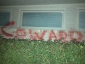 What looks like the side of a home is spray-painted with one word, "coward"