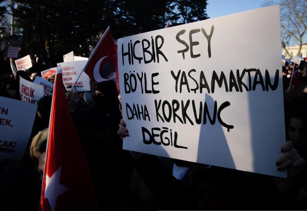 An unseen protestor holds a sign, which translated to english reads “Nothing is more horrible than living this way”